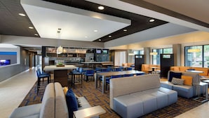 Un hall d’hôtel moderne doté d’un bar, de différents espaces de détente et offrant une vue sur l’extérieur.
