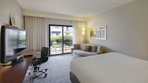 Une chambre d’hôtel avec un grand lit, un bureau avec une télévision, une chaise et un canapé.