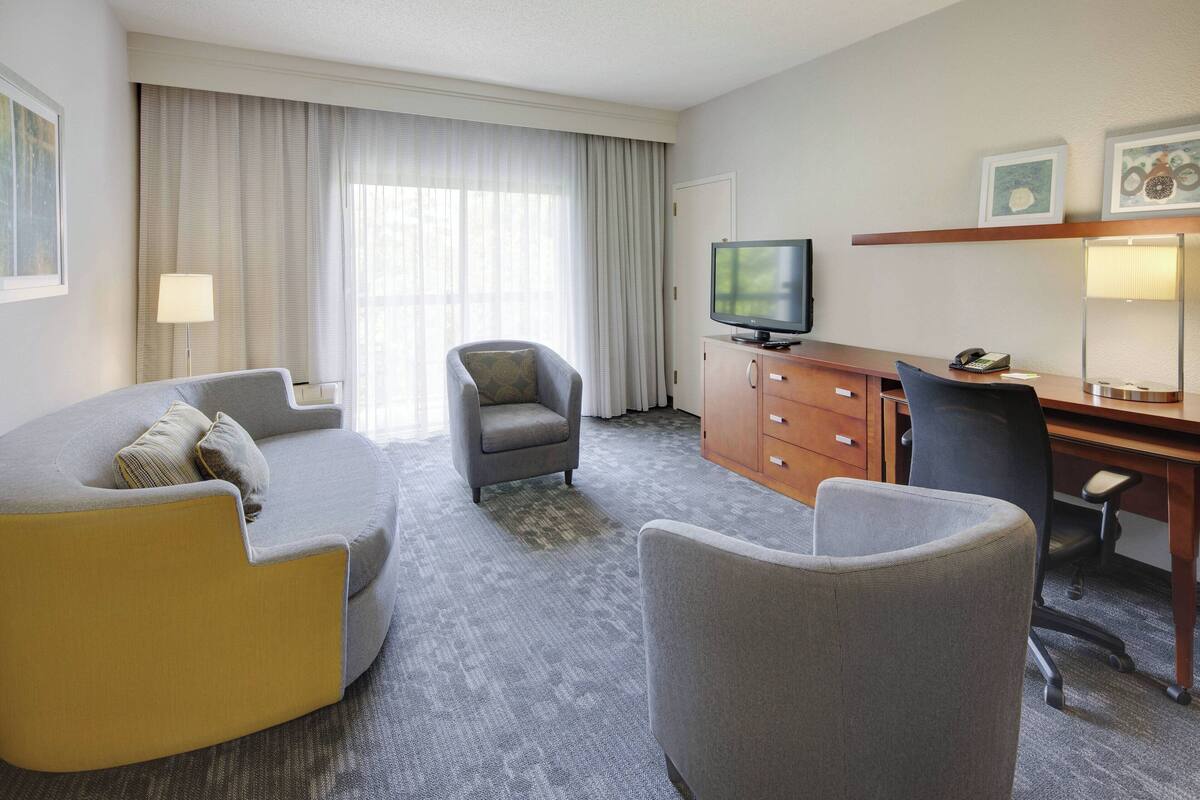 Een hotelkamer met een bank, fauteuil, bureau, televisie en een kast.