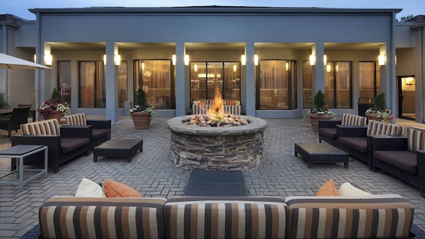 Un espace extérieur moderne, aménagé pour se détendre, avec un foyer en pierre, des canapés confortables et un patio couvert doté de grandes fenêtres.