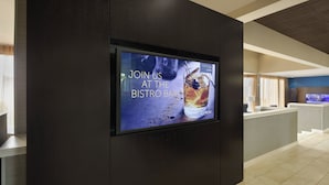 Un hall d’hôtel moderne doté d’un grand écran numérique affichant une invitation à visiter un bar-bistro.