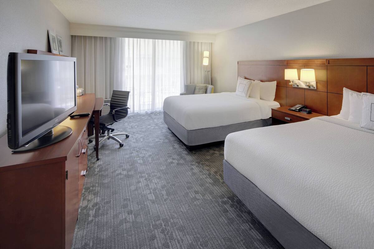 Een hotelkamer met twee bedden, een televisie, een bureau en een stoel.
