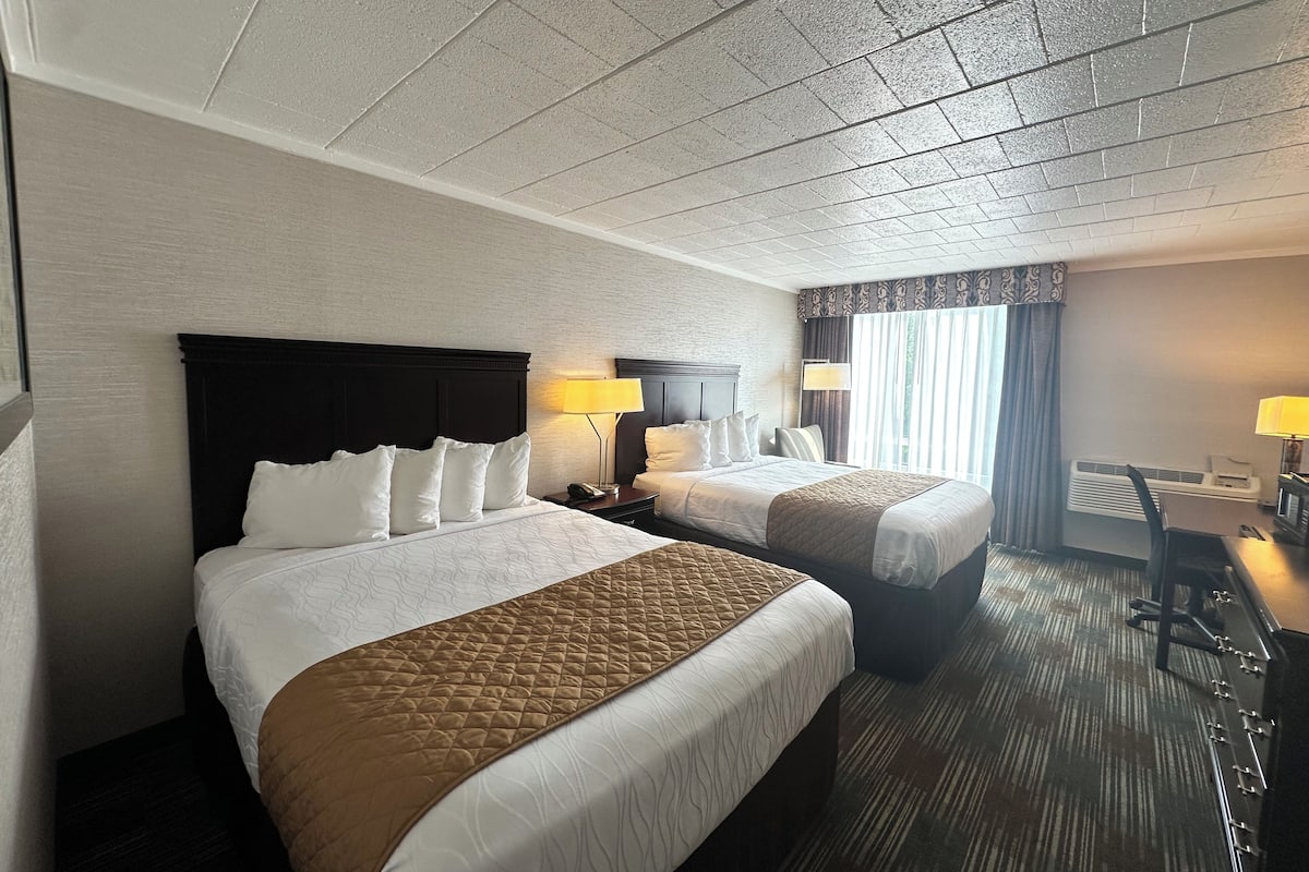 A hotel room with two beds, a desk, and a chair.