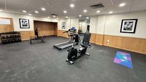 Een sportschool met loopbanden, een hometrainer en een bank.