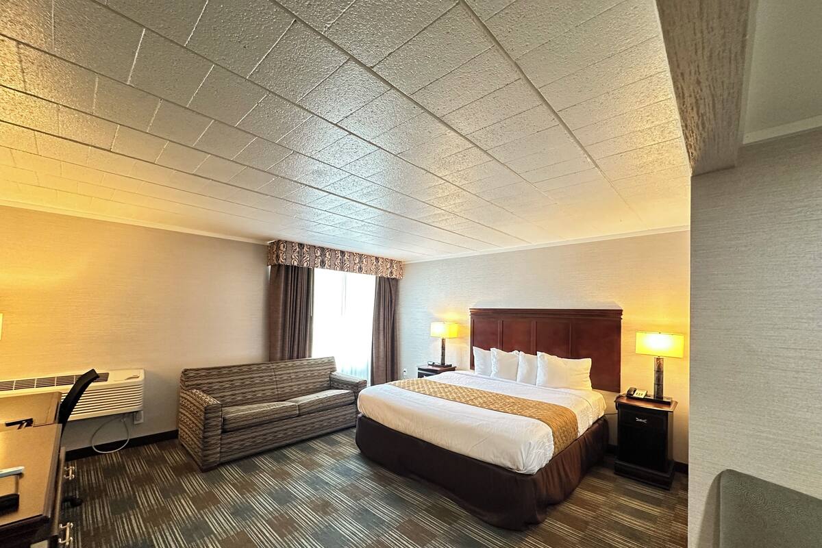 A hotel room with a large bed, a sofa, a desk with a lamp, and a window with curtains.