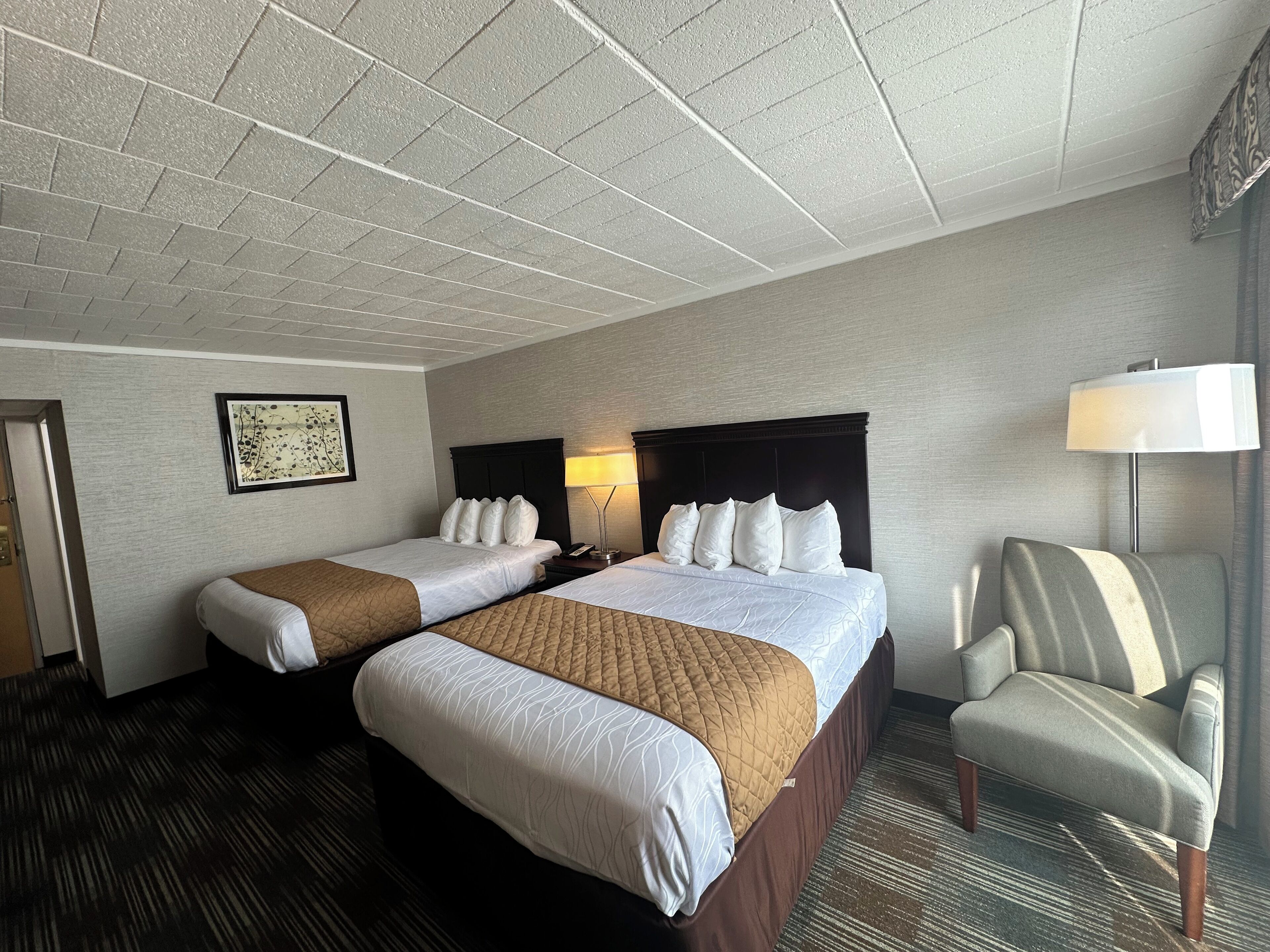 A hotel room with two beds, a chair, a lamp, and a framed picture on the wall.