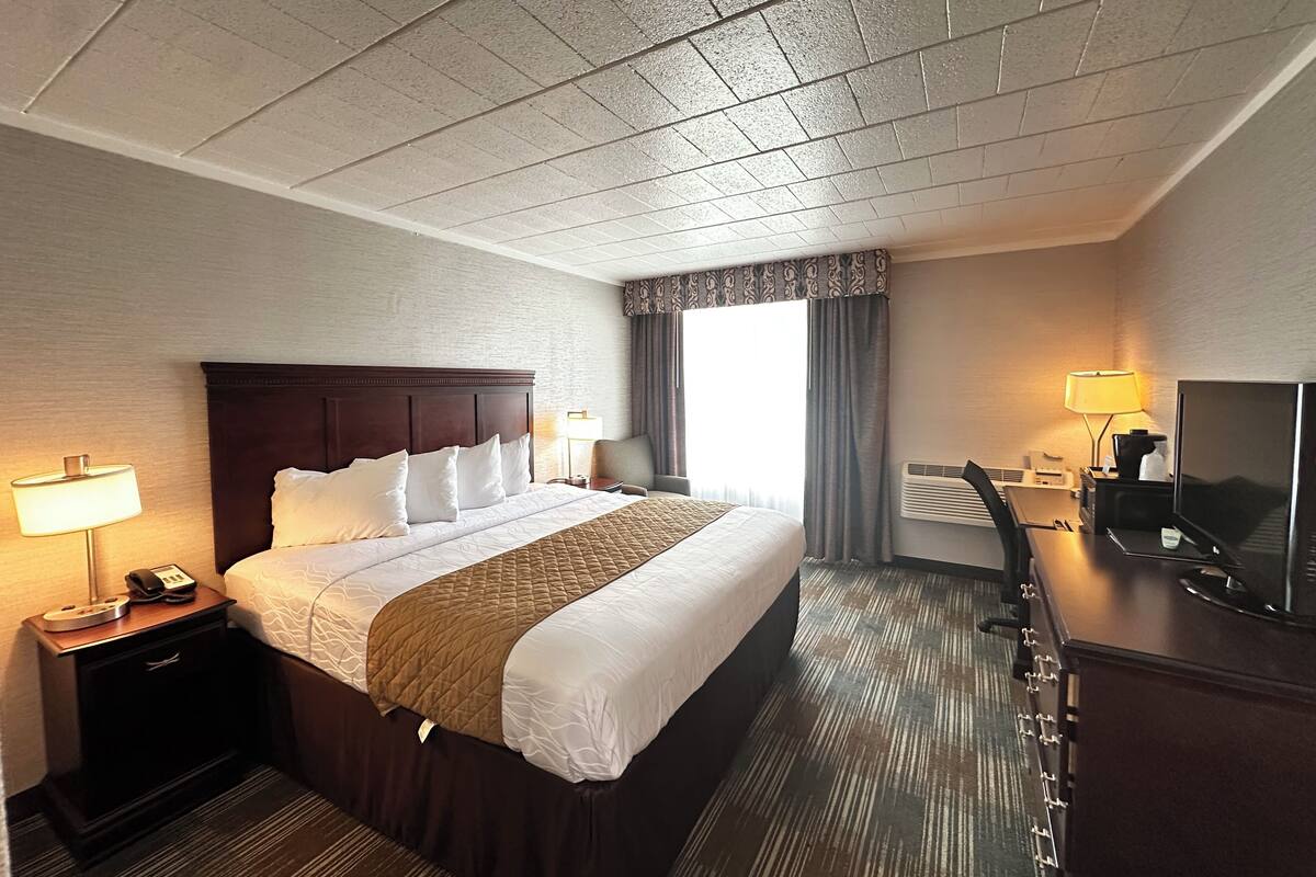 A hotel room with a large bed, a desk with a TV, a phone, and a lamp.