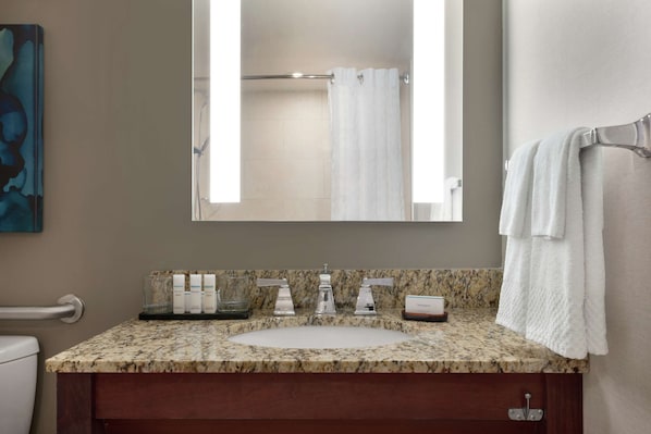 Un baño con encimera de granito, un lavabo blanco y un espejo que refleja una zona de ducha.