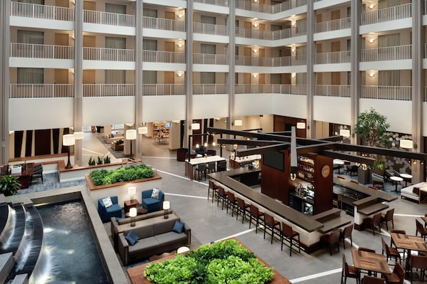 A multi-level hotel lobby with a central water feature, seating areas, a bar, and a reception desk.