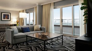 Quarto de hotel moderno com um sofá cinzento, uma mesa de centro de vidro e uma grande janela com vista para uma ponte.