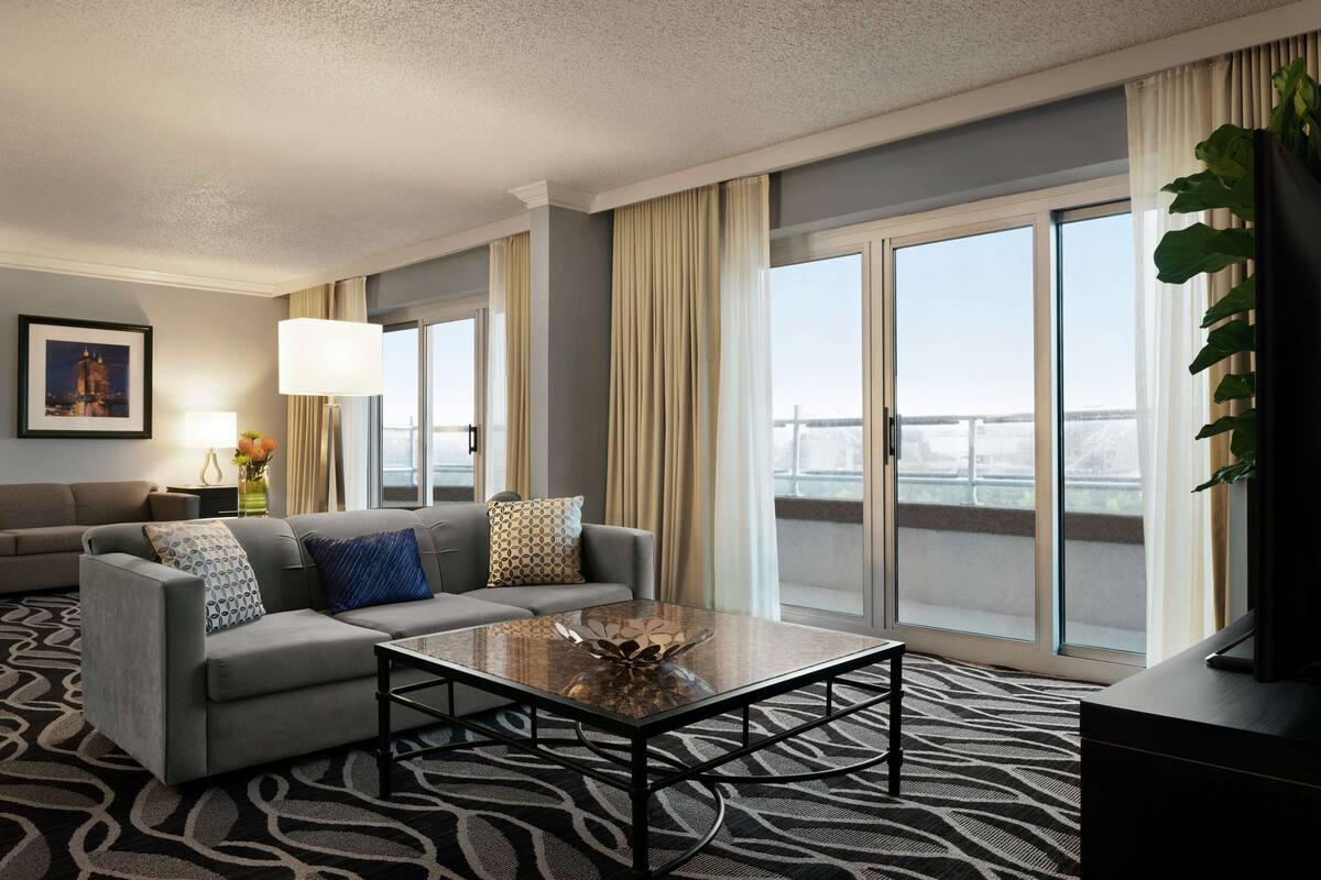 A modern hotel room with a grey sofa, a glass coffee table, and a large window with a view of a bridge.