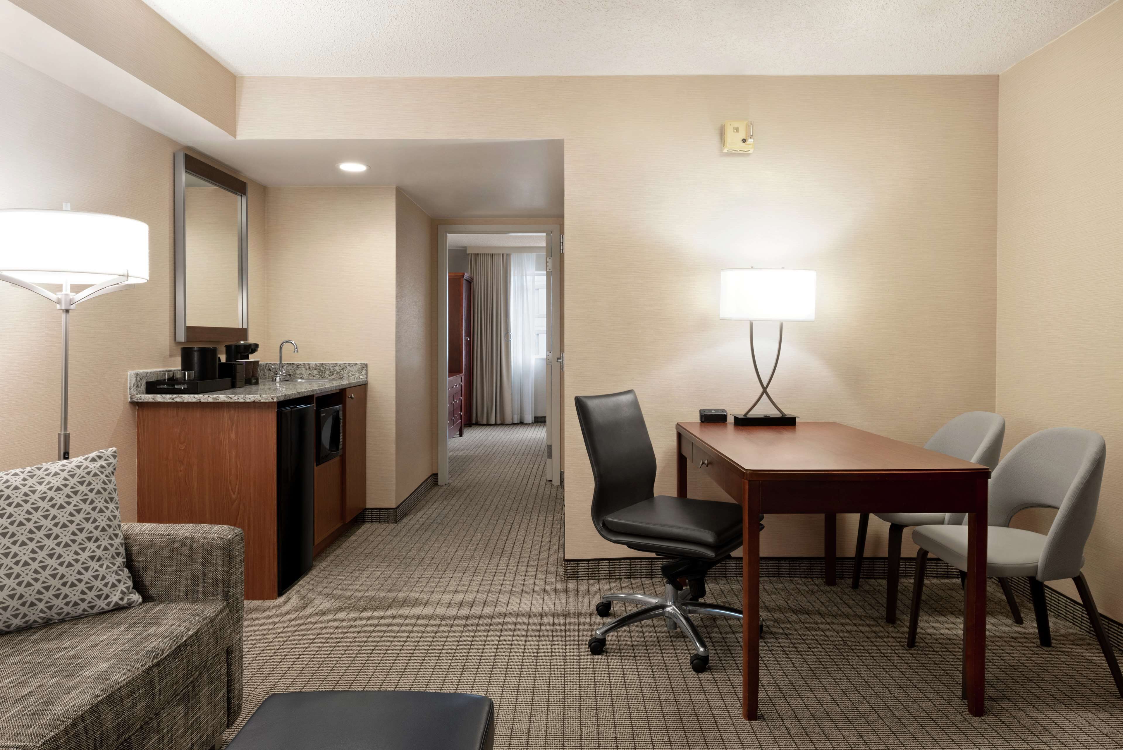 A hotel room with a kitchenette, a dining area with a table and chairs, a sofa, and a desk.