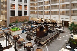 A spacious hotel lobby with multiple dining areas, a central bar, and a pool area.