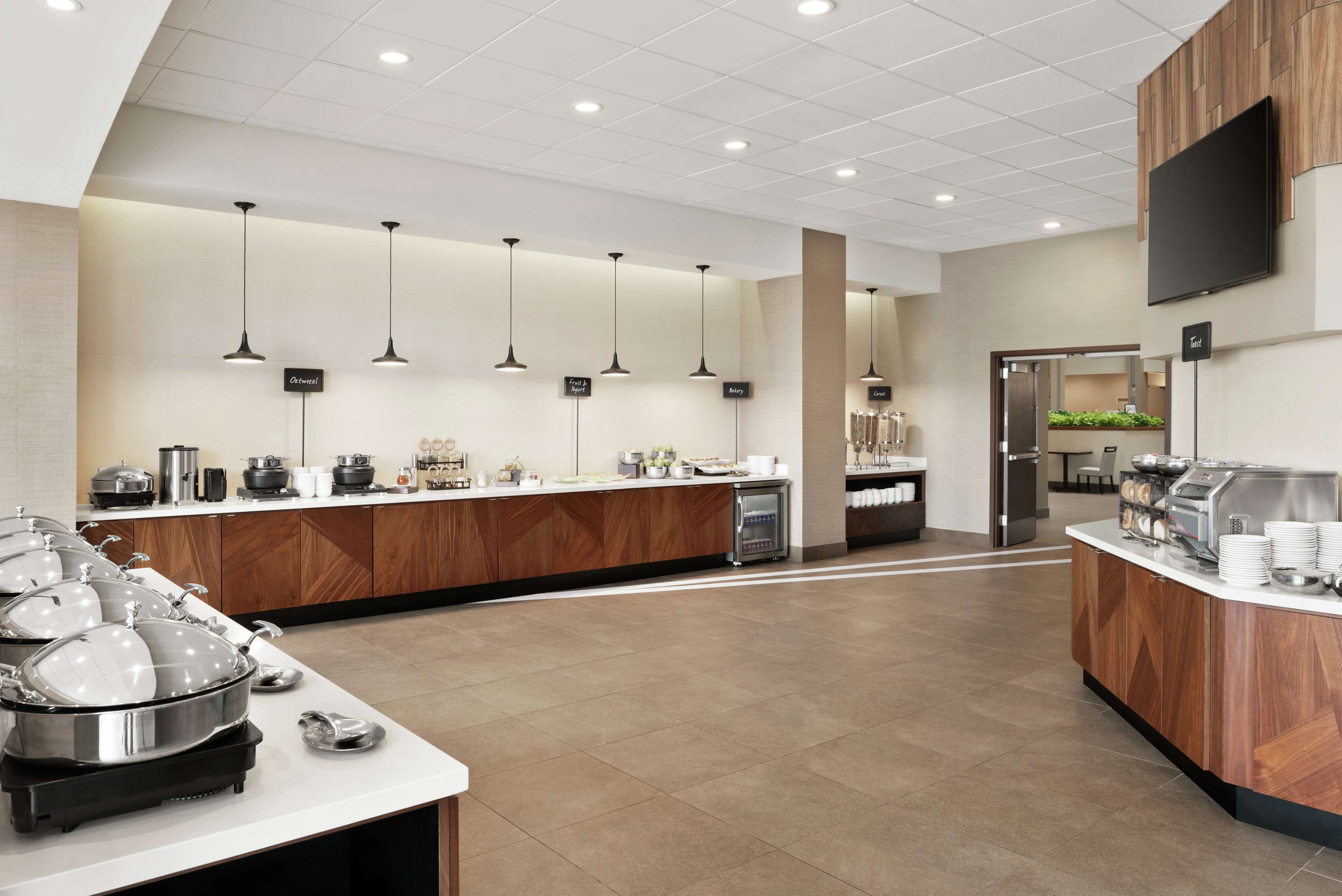 A modern buffet setup with multiple serving stations, a central island, and a flat-screen TV mounted on the wall.