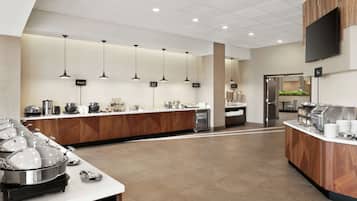 A modern buffet setup with multiple serving stations, a central island, and a flat-screen TV mounted on the wall.