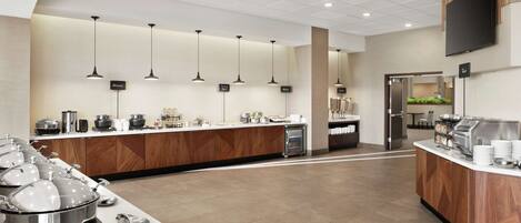 A modern buffet setup with multiple serving stations, a central island, and a flat-screen TV mounted on the wall.