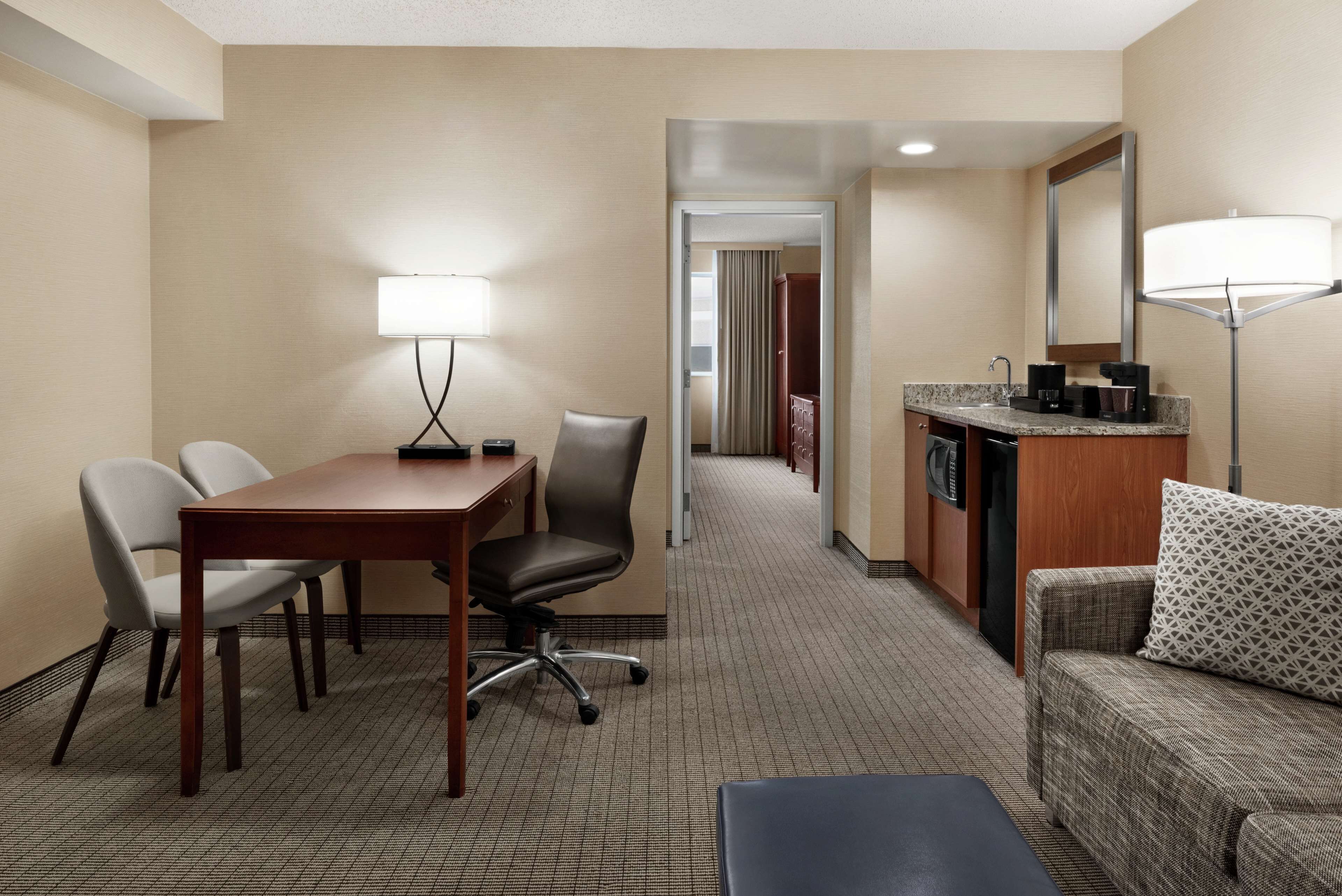 Habitación de hotel con una mesa de comedor, dos sillas, un sofá, una pequeña mesa de centro, una kitchenette y un espejo.