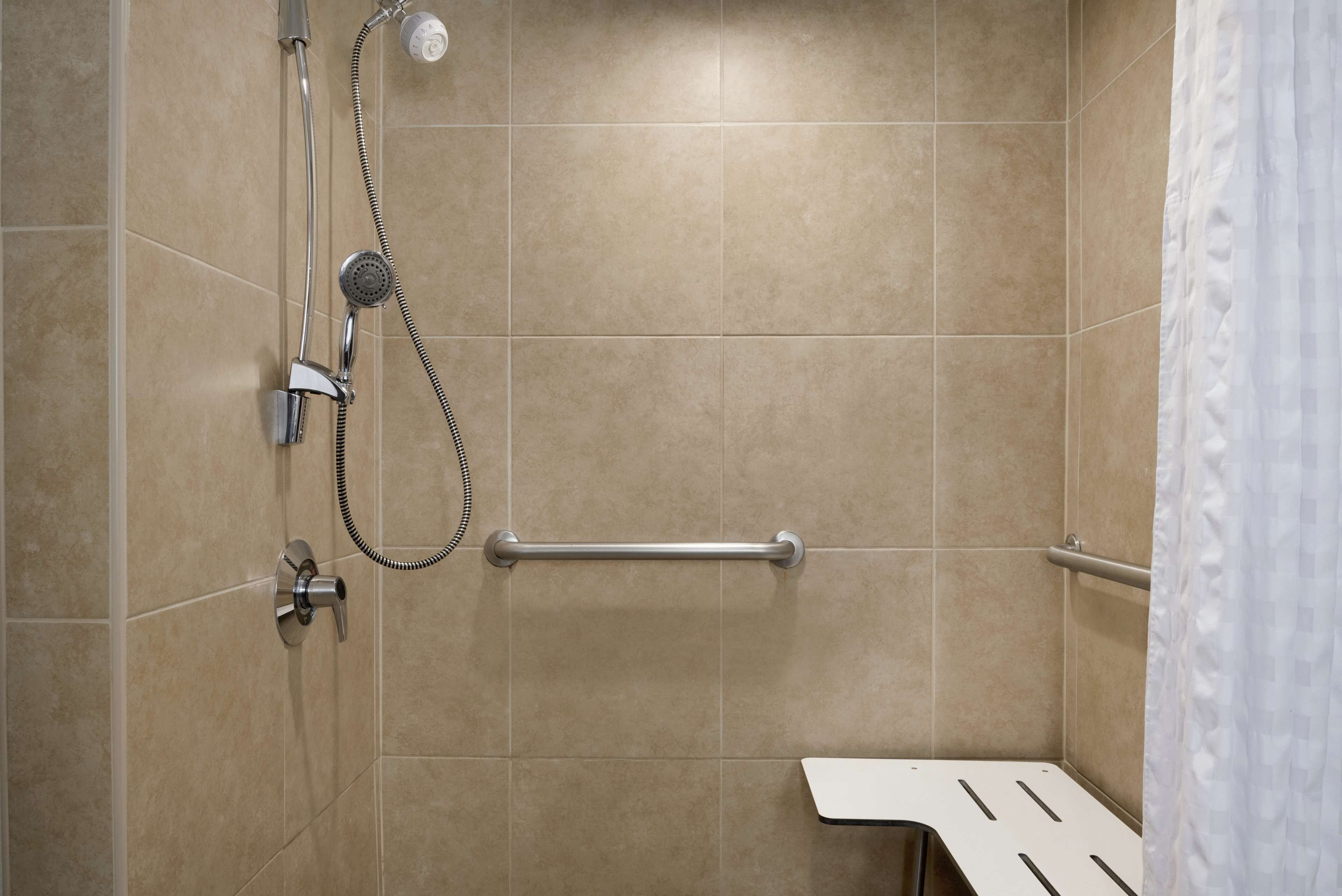 A shower area with a handheld showerhead, a handheld shower attachment, and a grab bar.