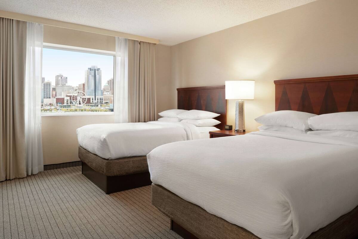 A hotel room with two beds, a city view, and a lamp on the nightstand.