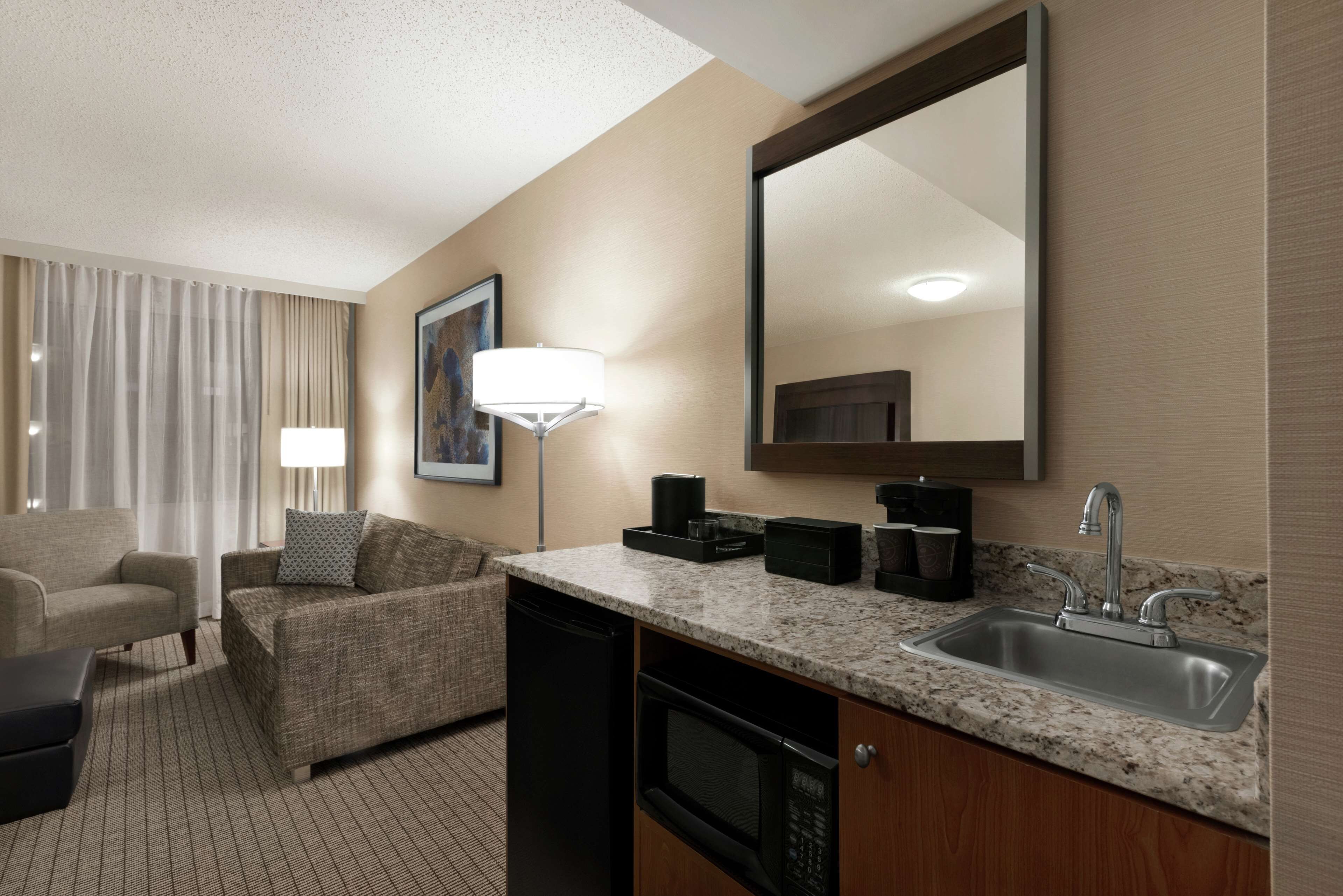 A hotel room with a kitchenette, a sofa, a dining table, and a large mirror.