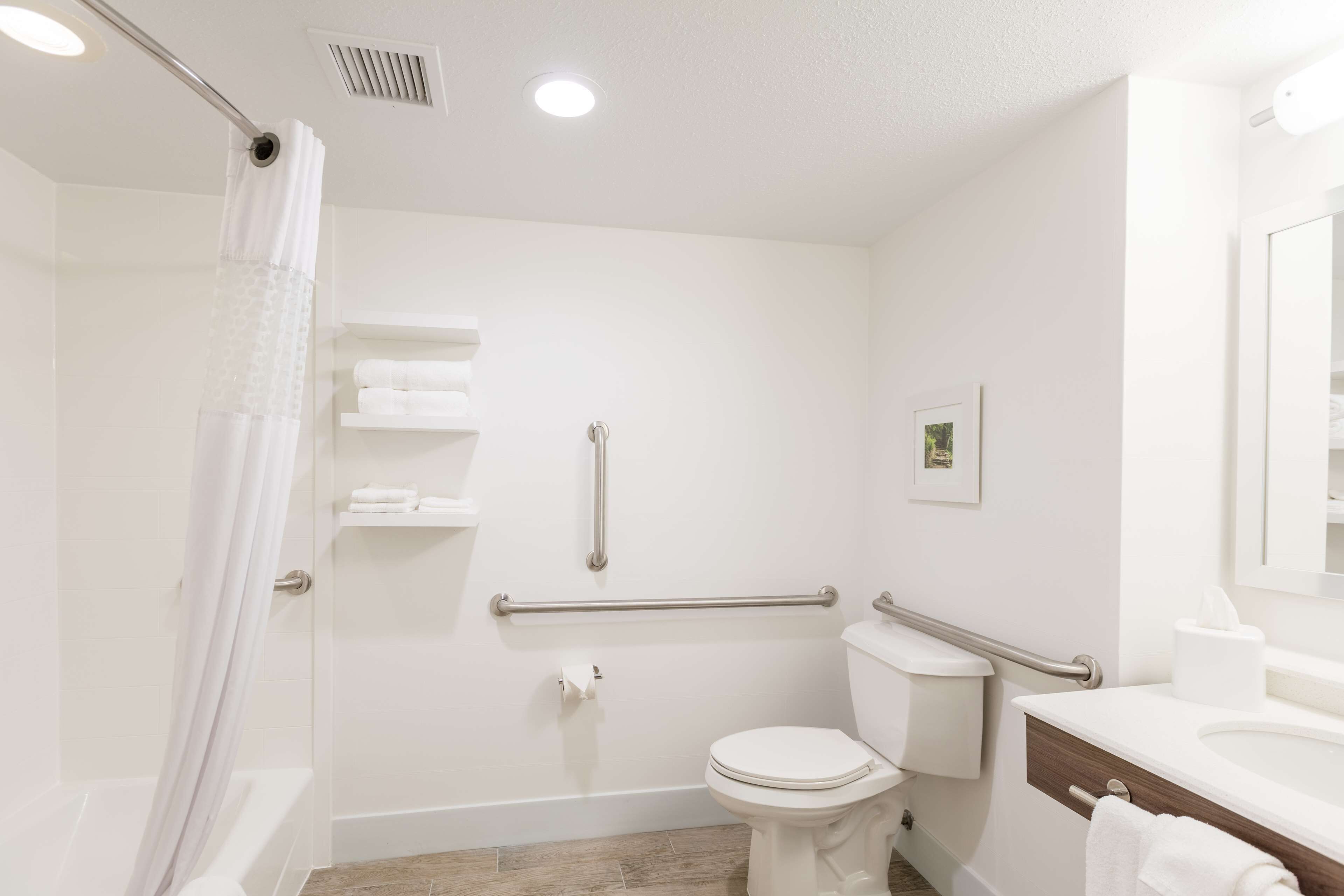 A modern bathroom with a shower, toilet, and sink. It includes grab bars and a towel rack.
