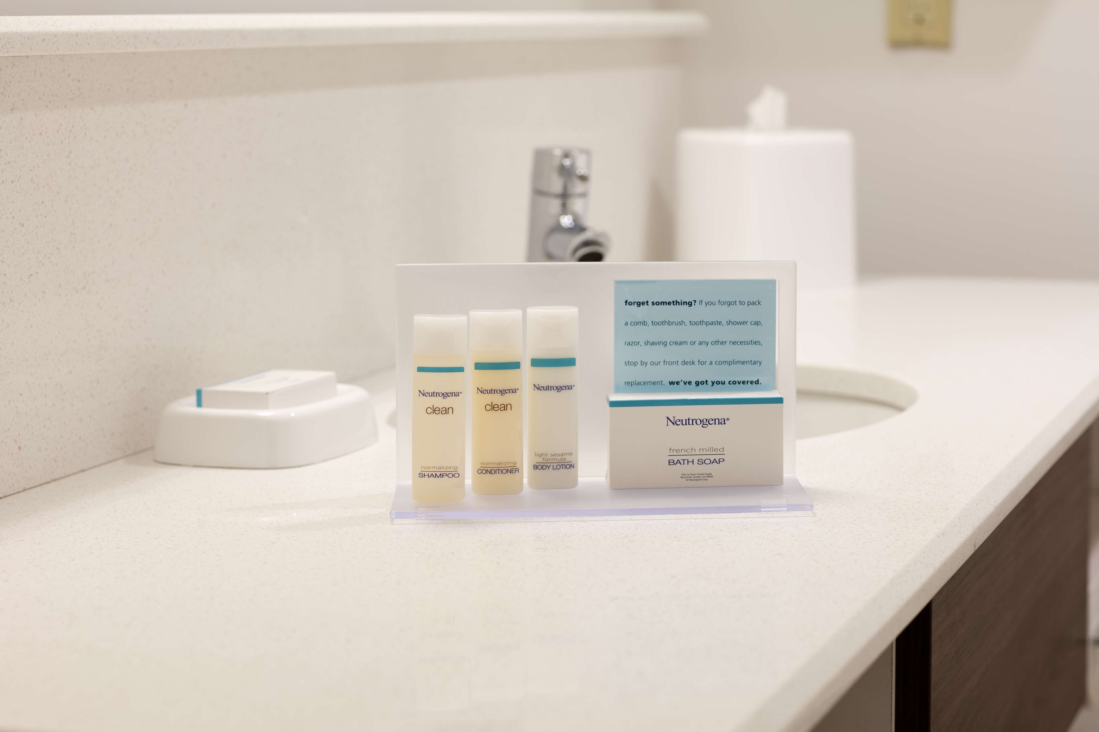 Un lavamanos de baño con tres productos Neutrogena: champú, acondicionador y crema corporal, y un letrero que ofrece un reemplazo de cortesía.