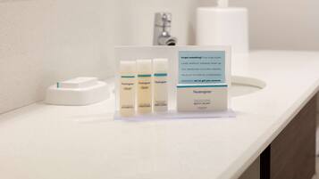 Un lavamanos de baño con tres productos Neutrogena: champú, acondicionador y crema corporal, y un letrero que ofrece un reemplazo de cortesía.