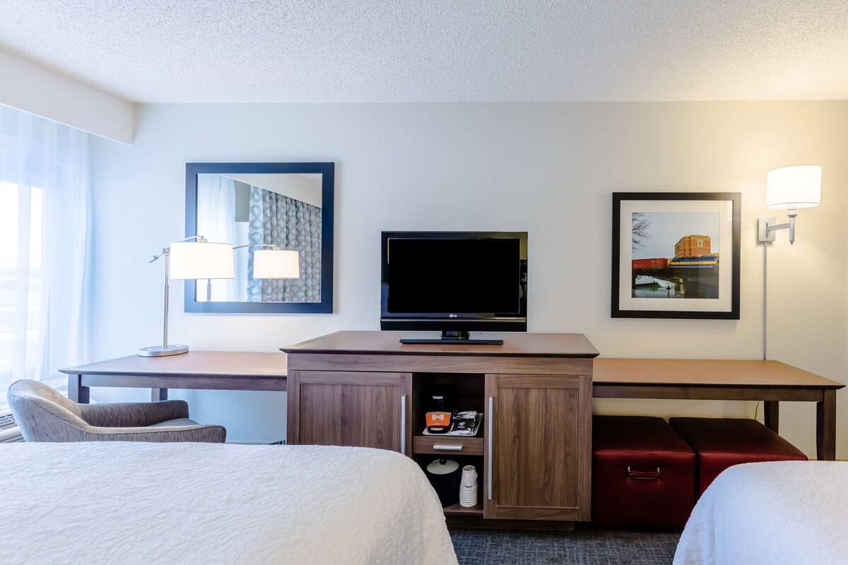 A hotel room with a bed, a desk with a TV, a lamp, and a framed picture on the wall.
