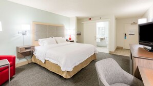 A hotel room with a bed, a desk, a chair, a TV, and a bathroom visible through an open door.