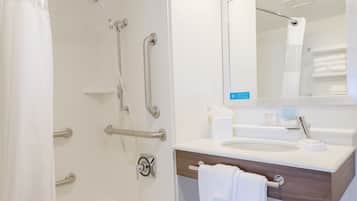 A modern bathroom with a walk-in shower, grab bars, a vanity with a mirror, and a white towel hanging on the wall.