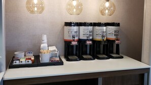 A coffee station with four coffee dispensers, a stack of disposable cups, and a tray with various coffee-related items.