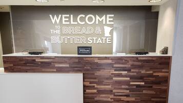 A reception desk with a 'Welcome to the Bread & Butter State' sign, a wooden panel design, and a 'Hilton Honors' logo.