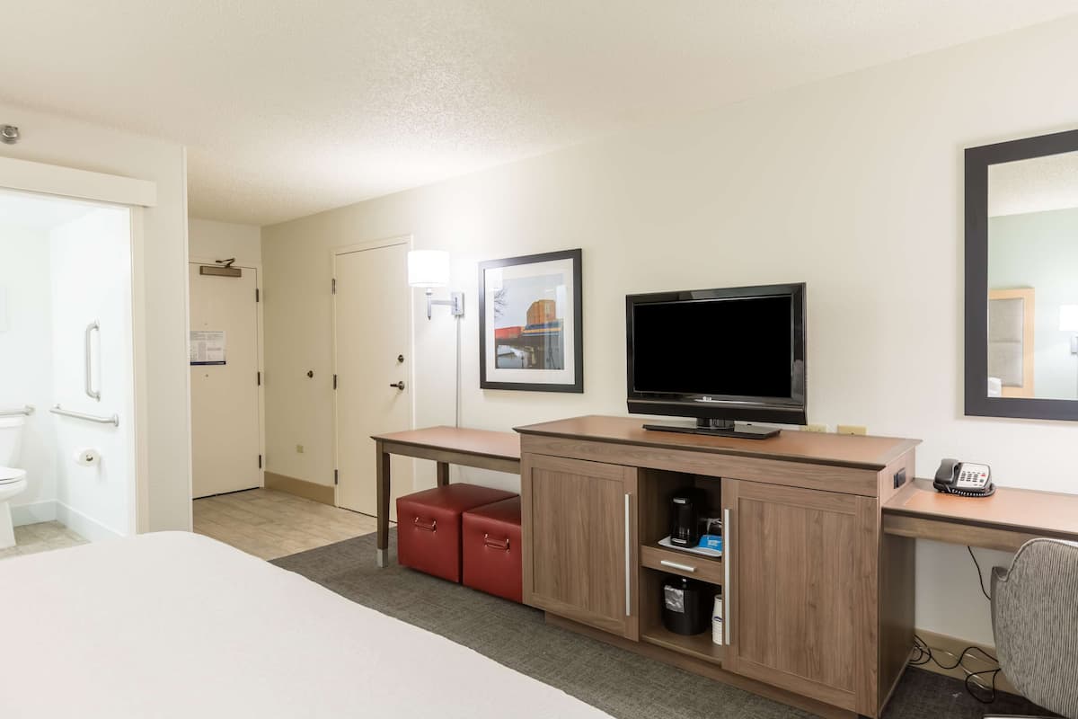 A hotel room with a bed, a desk with a television, a phone, and a small red storage unit.