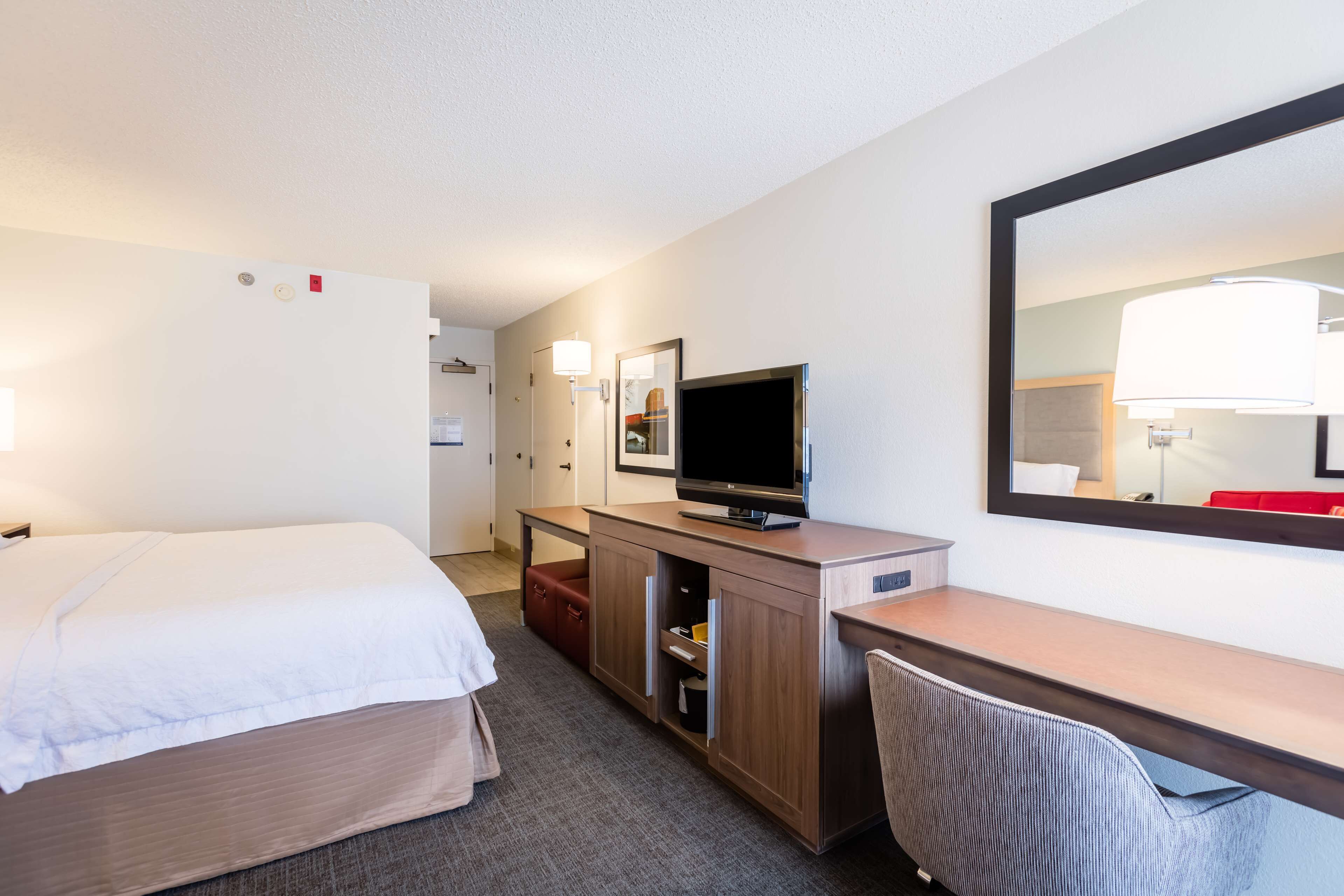 A hotel room with a bed, a desk, a television, a mirror, and a red chair.