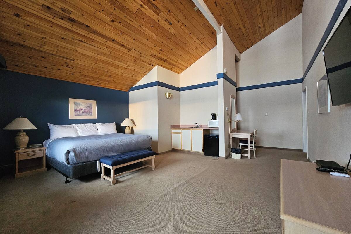 A bedroom with a bed, bedside tables, a desk, a chair, and a television.
