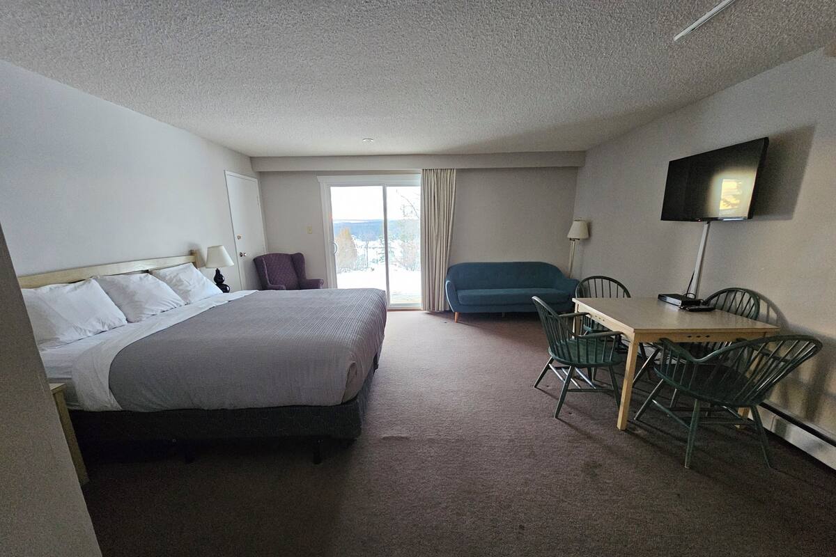 A hotel room with a bed, a desk with chairs, a TV, and a view of the outdoors.