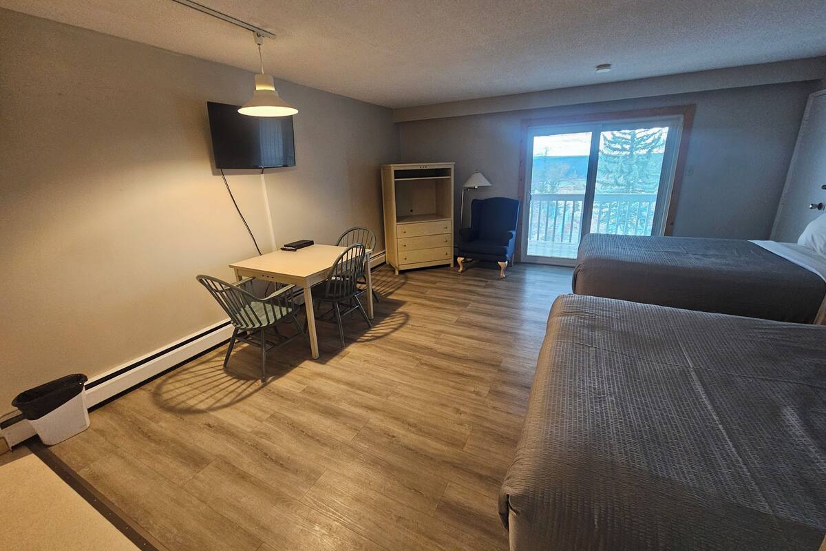 A room with a bed, a desk, a chair, a TV, and a window with a view.