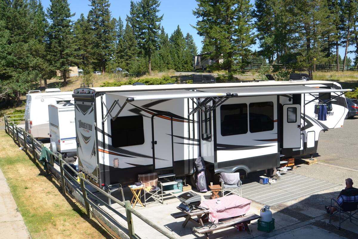 A recreational vehicle (RV) parked in a campsite with a covered picnic area, a grill, and a portable toilet.