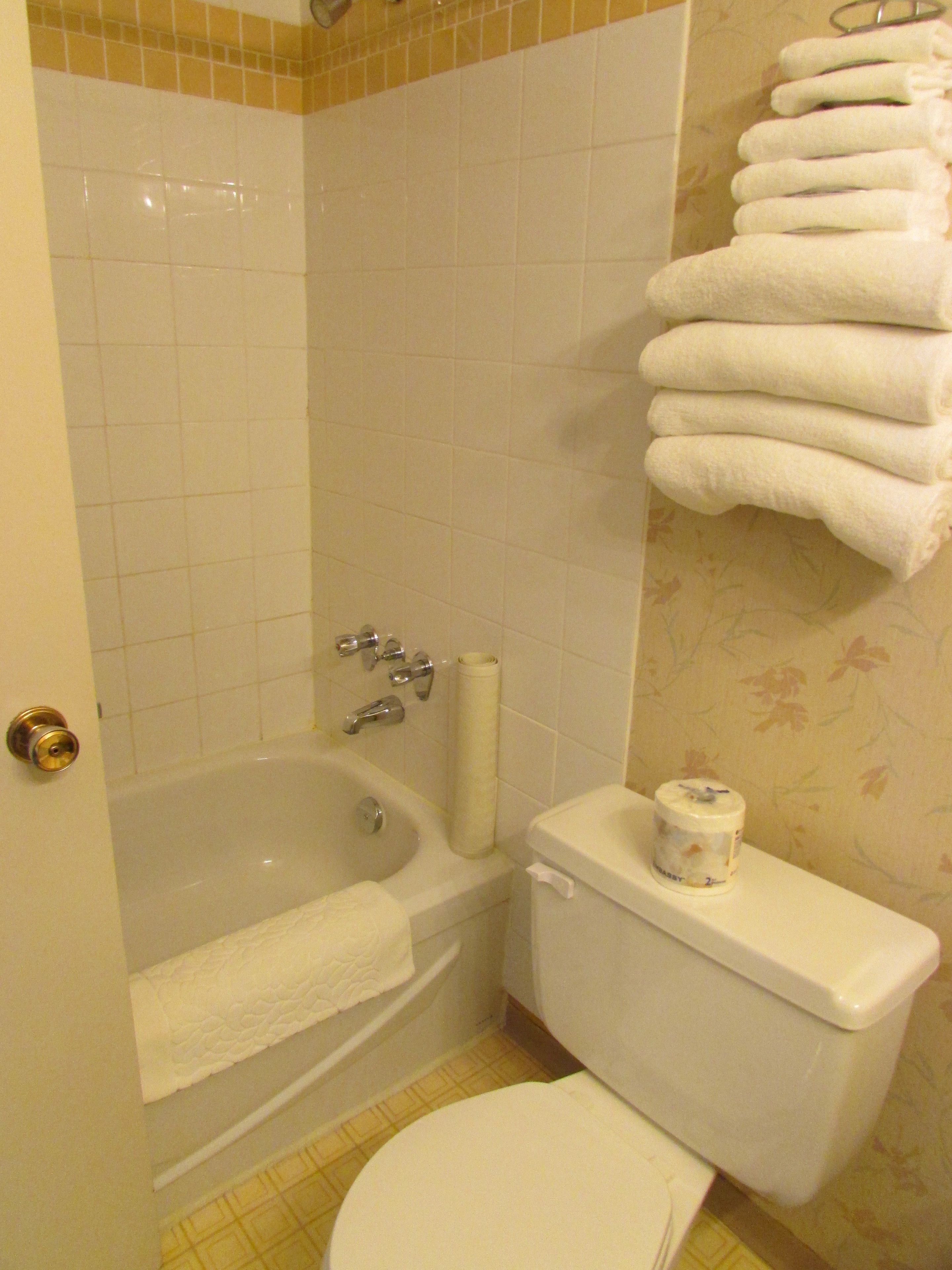 A bathroom with a bathtub, toilet, and a towel rack with folded towels.