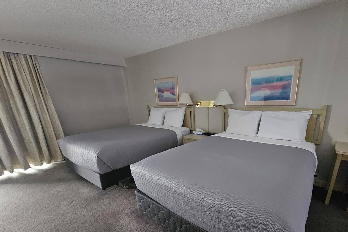A hotel room with two beds, a nightstand, a lamp, and a window with curtains.