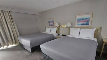 A hotel room with two beds, a nightstand, a lamp, and a window with curtains.