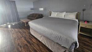 A bedroom with a large bed, a bedside table, a lamp, a chair, and a wooden floor. - 108 Golf Resort (108 Mile Ranch)