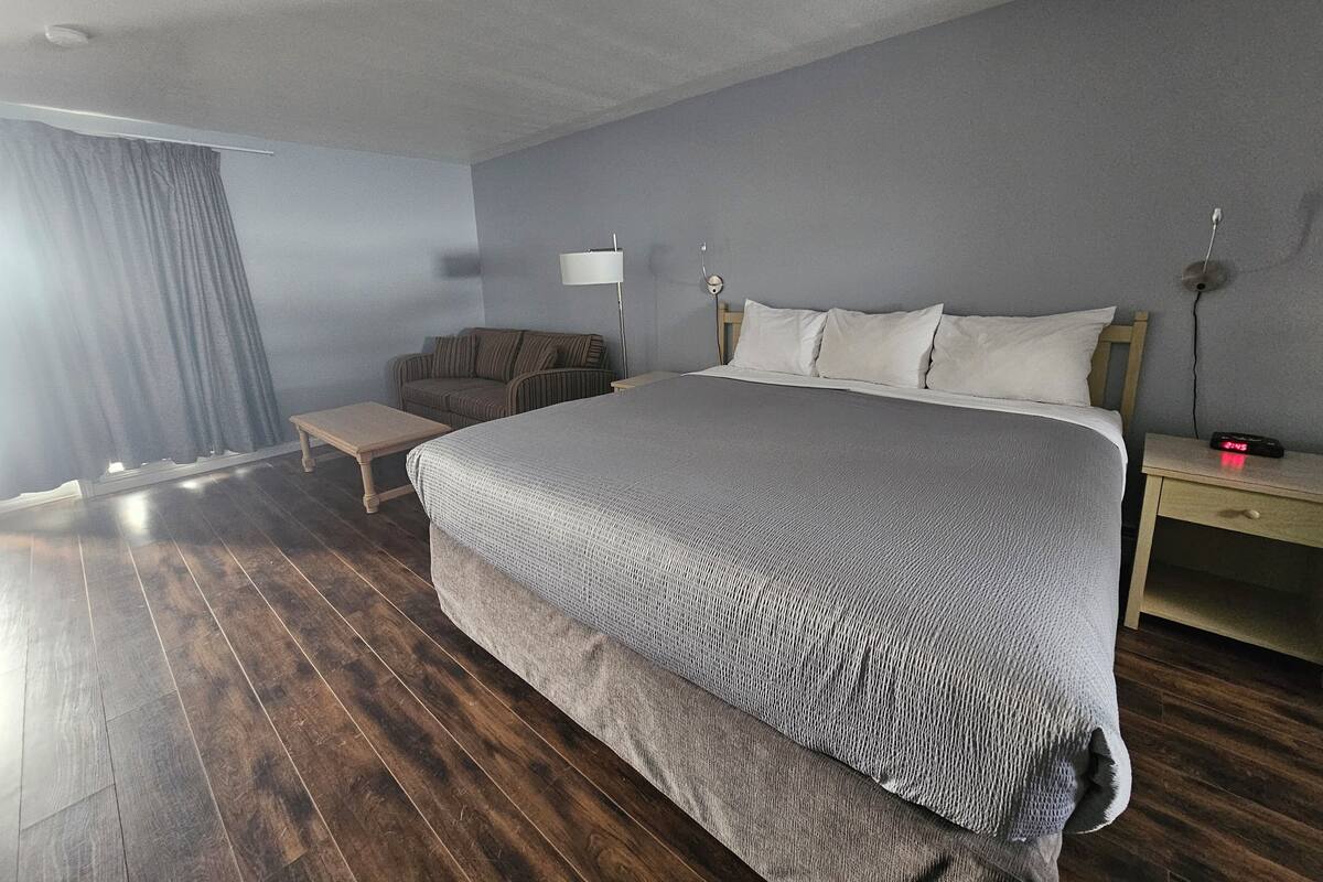 A bedroom with a large bed, a bedside table, a lamp, a chair, and a wooden floor.