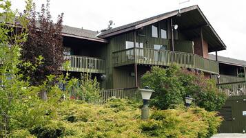A multi-story building with balconies and a garden area in front.