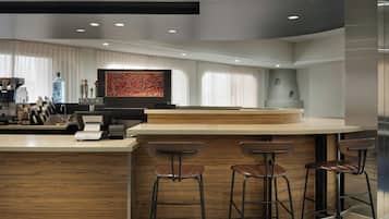A modern bar area with a wooden counter, bar stools, and a large abstract painting on the wall.