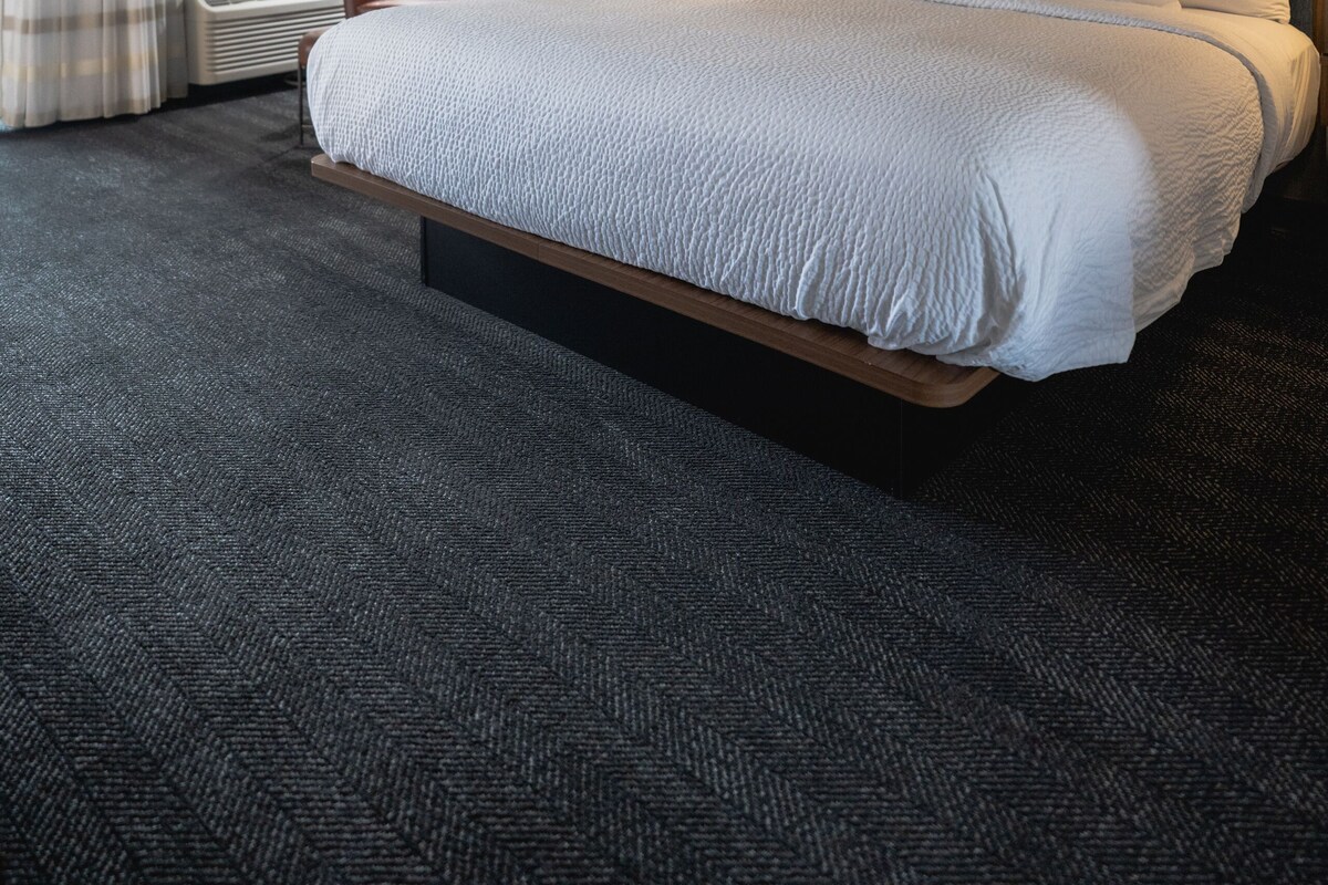 Una habitación de hotel con una cama grande, una silla, un escritorio con lámpara y una ventana con cortinas.