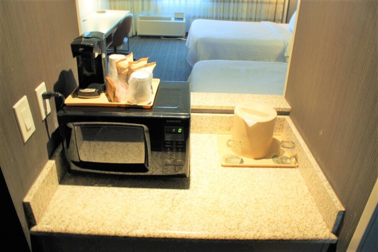 Una kitchenette compacta con microondas, cafetera y una taza de café sobre una bandeja.
