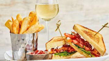 A plate with a grilled sandwich, a glass of white wine, and a container of fries.