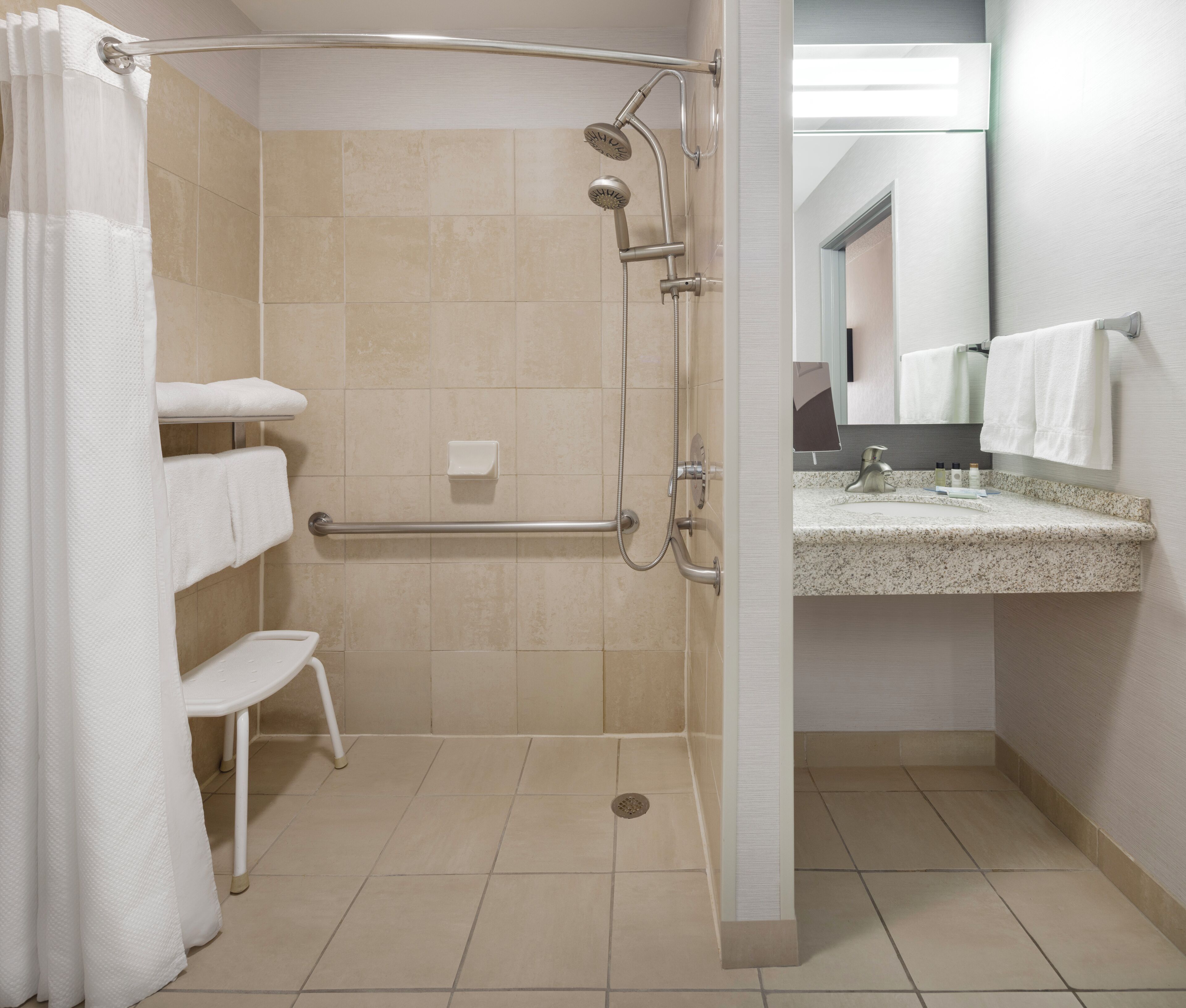A modern bathroom with a shower, a handrail, a sink with a mirror, and a towel rack.