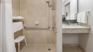 A modern bathroom with a shower, a handrail, a sink with a mirror, and a towel rack.